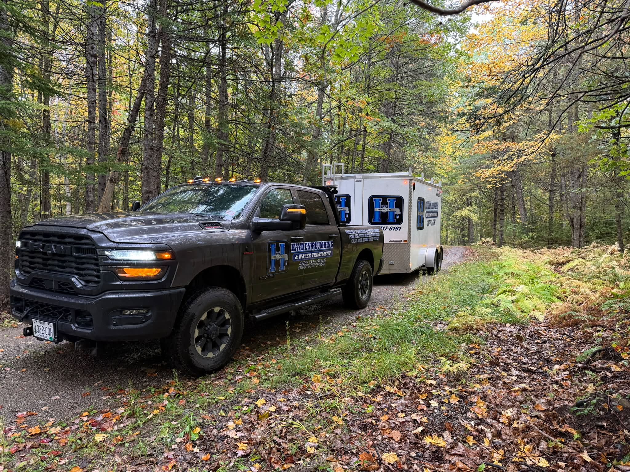 Hayden Plumbing service truck and trailer on a wooded Maine road